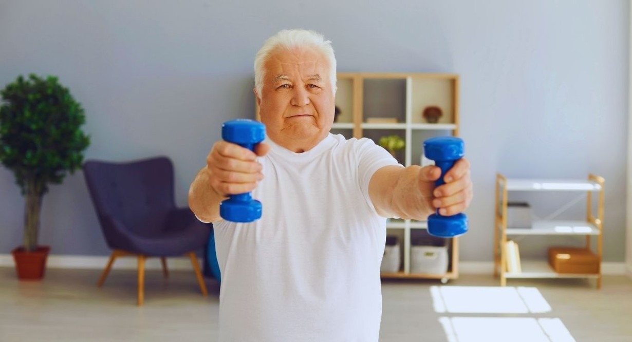 Homme senior tenant deux haltères bras tendus lors d'une séance de sport dans son salon